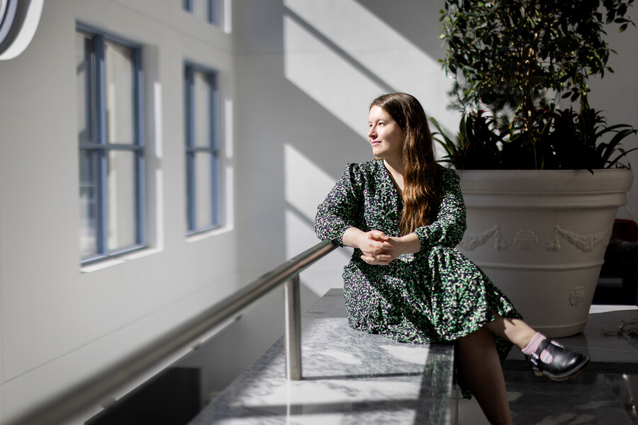 Olena Lysenko sits on a bench looking over her right shoulder out a window, hands clasped and legs crossed.