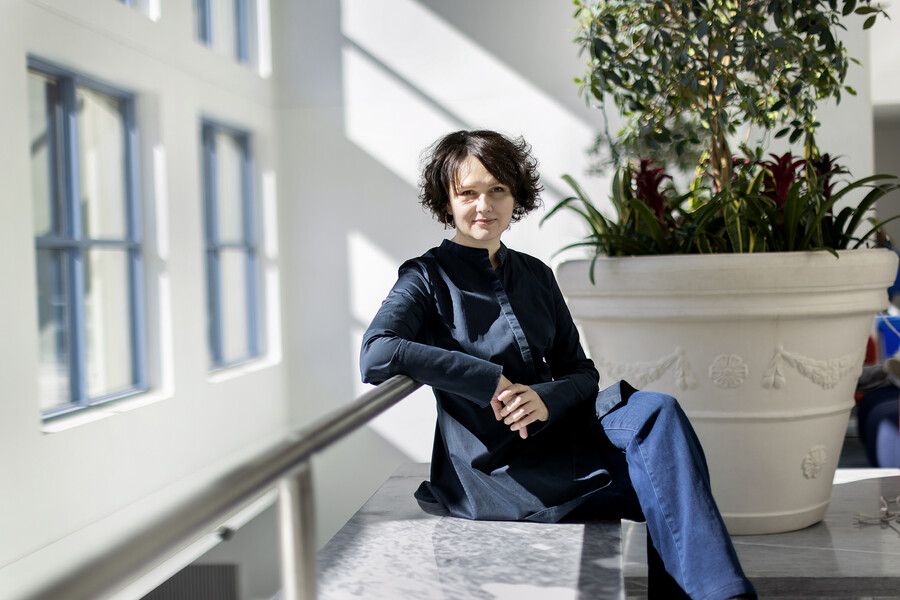Dariya Orlova sits on a bench, hands clasped, elbow resting on a bar, and legs crossed.