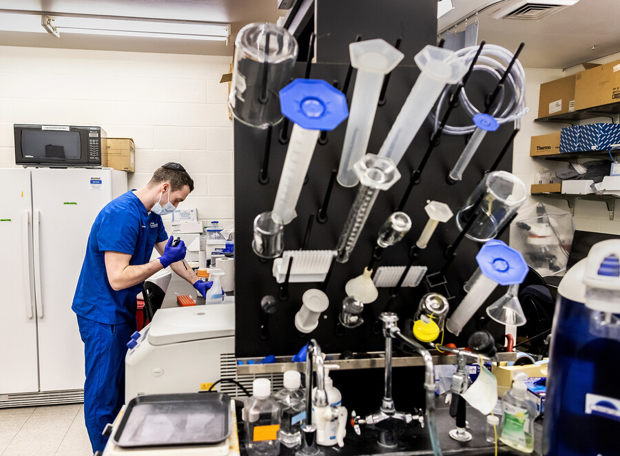 scientist in scrubs pipets a liquid in a lab with many beaker drying on a rack over a sink