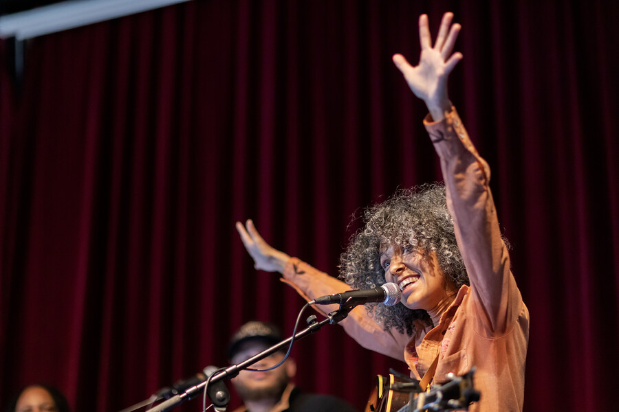 A singer and guitarist seated on a stool puts their hands in the air in WXPN’s studio.