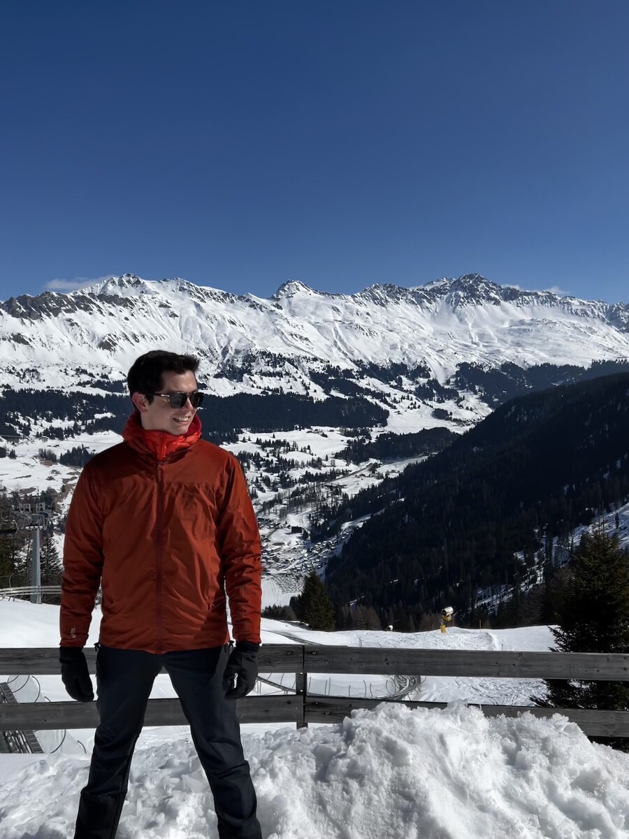 Ricardo de Rio stands in front of a snowy mountain range in Switzerland.