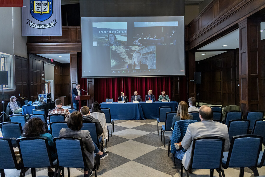 Person at podium and panelists speak to audience at event in large hall