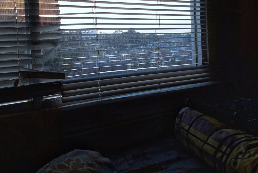 View of a city out of broken blinds from a bedroom.