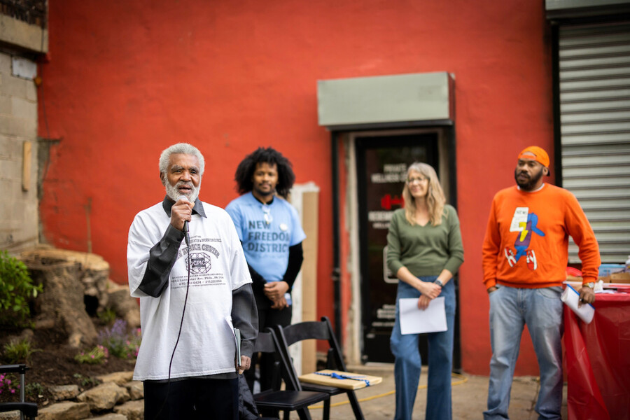 Muhamed Kenyatta speaking into a microphone while three people look on.
