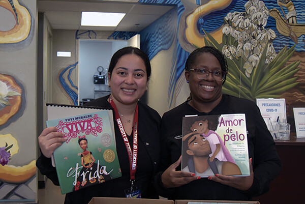 Two people holding up children’s books written in Spanish.