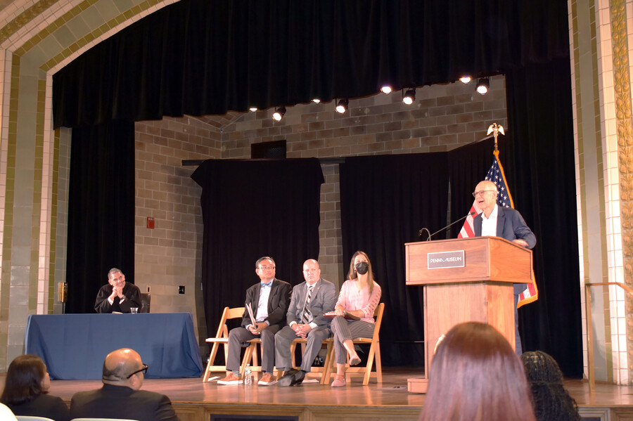 Ezekiel Emanuel stands at a podium on a stage in front of an American flag as four other people on the stage look on.
