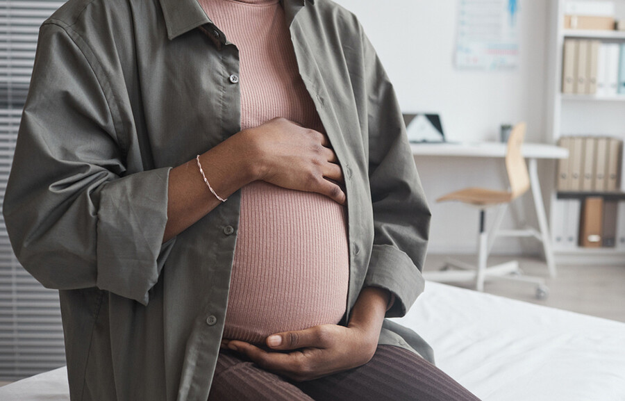 Pregnant person holding their belly in a doctor’s office.