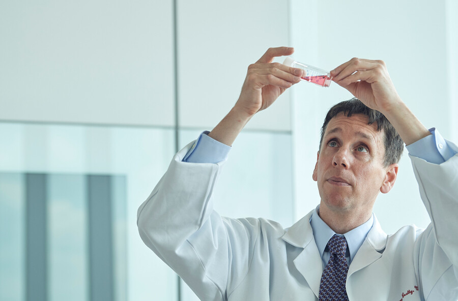 Gregory Beatty holds up a lab sample in a lab coat.