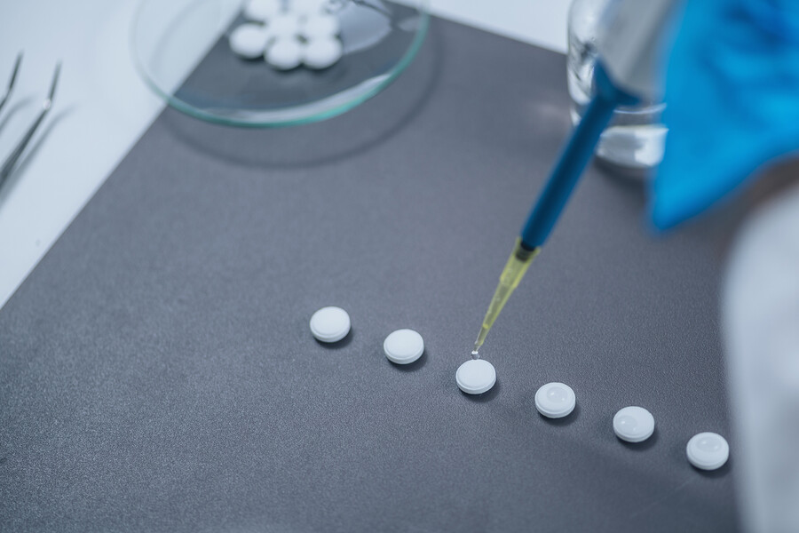 A gloved hand dripping a substance from a pipette onto pills.