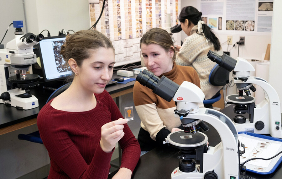 Two students looking at slides under a microscope in a lab.