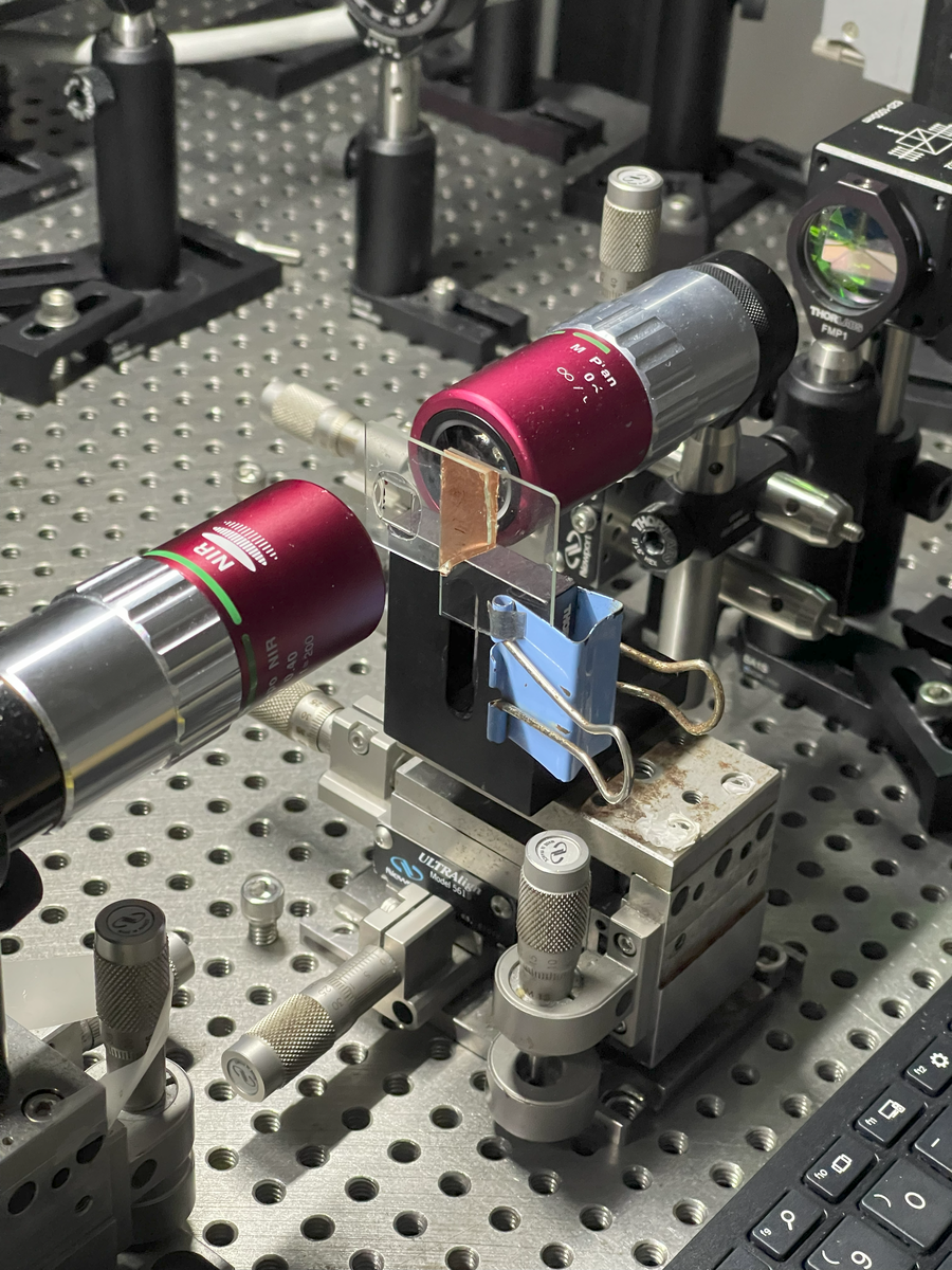 Close-up of two lenses aimed at a glass sample on a metal mount for quantum optics experiments.