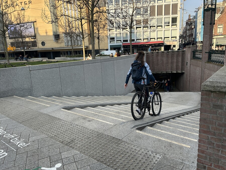 A person using a walking ramp for their bicycle to descend an outdoor staircase.