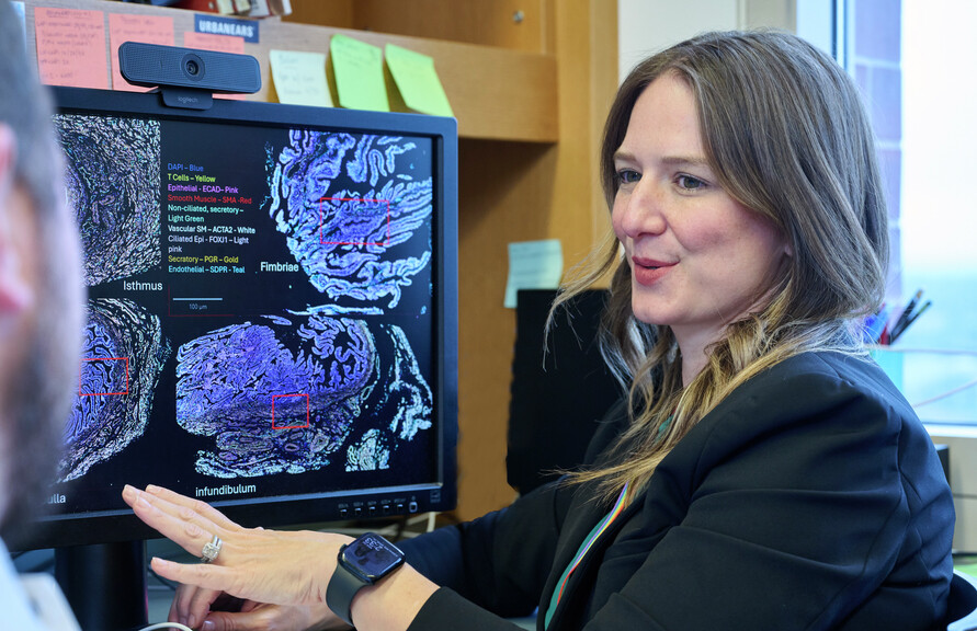 Kathleen O’Neil speaking with someone at her desk with a medical scan on her computer screen.
