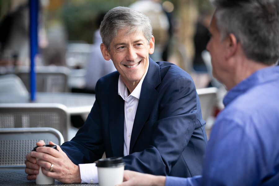 Tom Murphy grips a coffee while sitting at a table with a colleague.