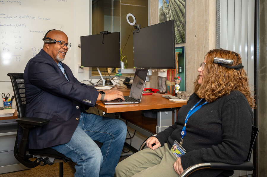 Kevin Johnson seated at his desk with a computer and Karen O'Connor, seated at his desk, both testing the new equipment.