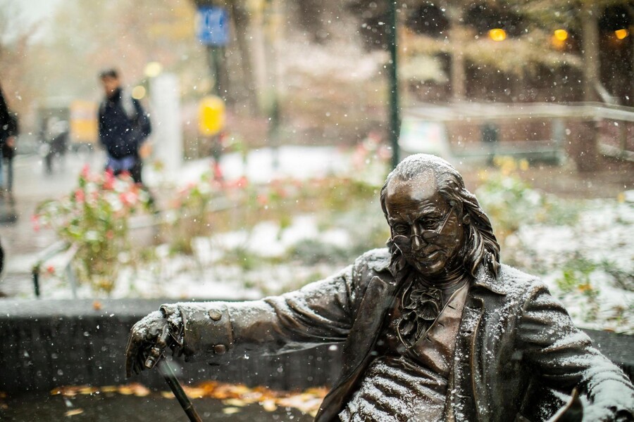 Statue of Ben Franklin on a bench in the snow.
