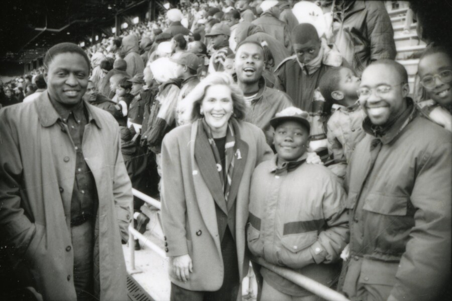 Glenn Bryan (left), Judith Rodin (center), and local community members (on the right) in a stadium environment, all smiling and facing forward.