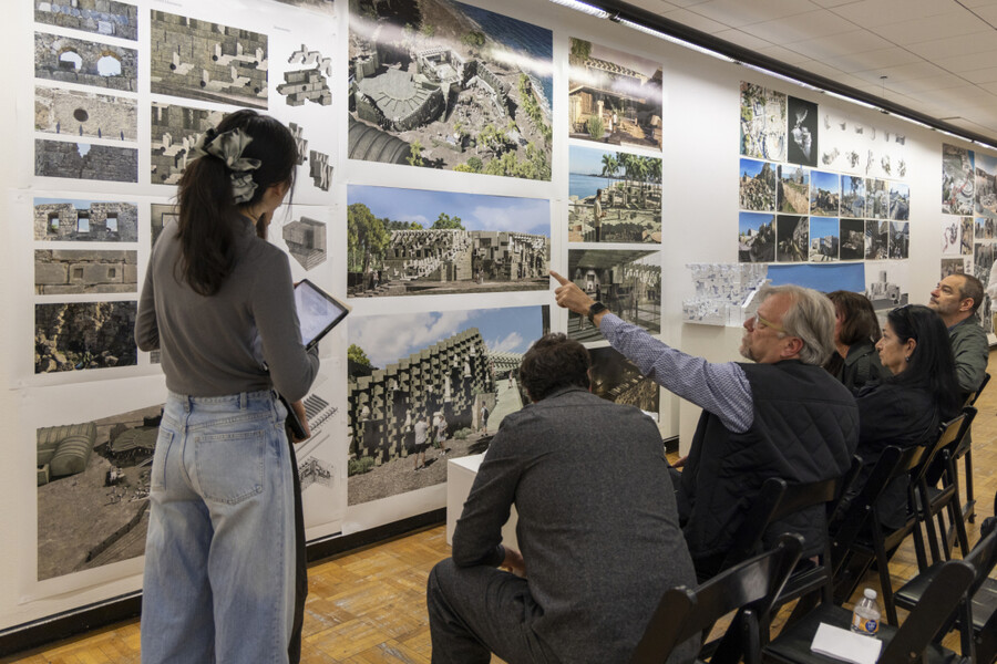 Ferda Kolatan (seated far right) in his studio pointing to photographs on the wall with onlookers.