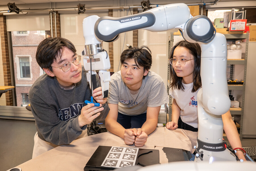 Three students working on a robotic arm in the GRASP lab
