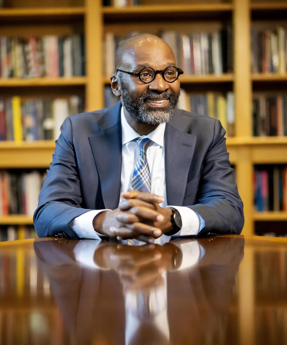 John Jackson rests his hands on a table in front of a bookcase.