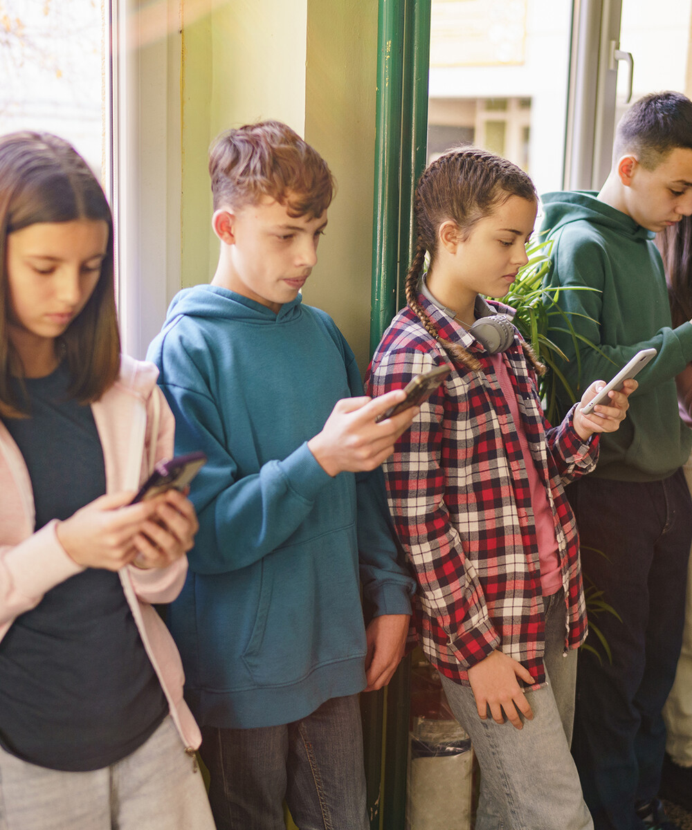 A group of middle-school kids in a hallway all looking at their phones.