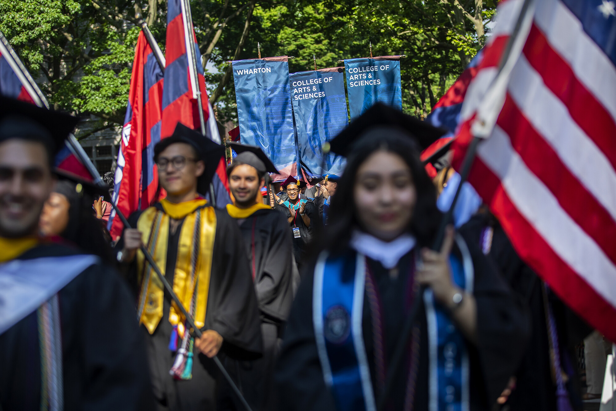 Graduates holding flags in procession down Locust Walk.