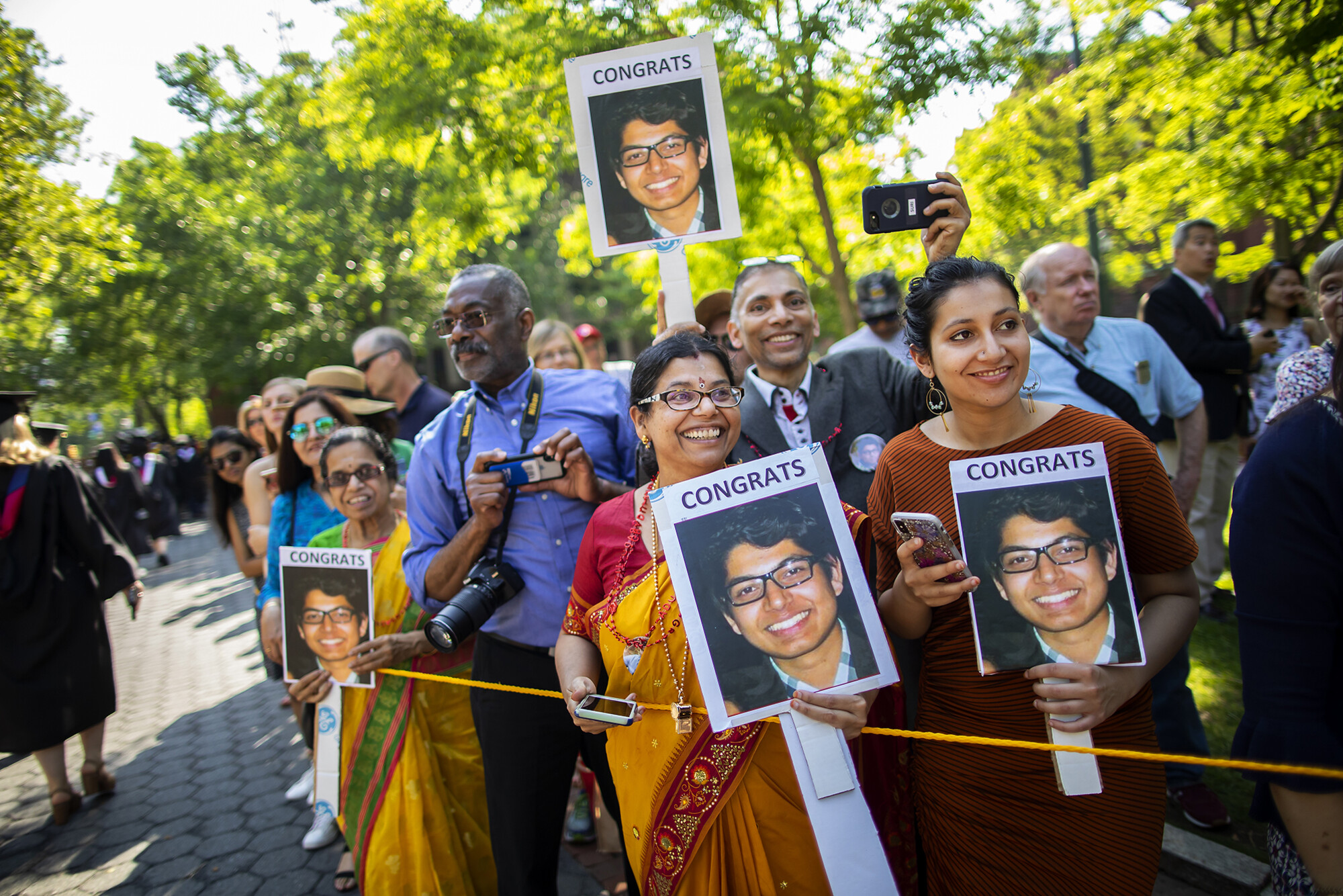 Family members hold pictures of a graduate that read CONGRATS along Locust Walk while snapping photos.