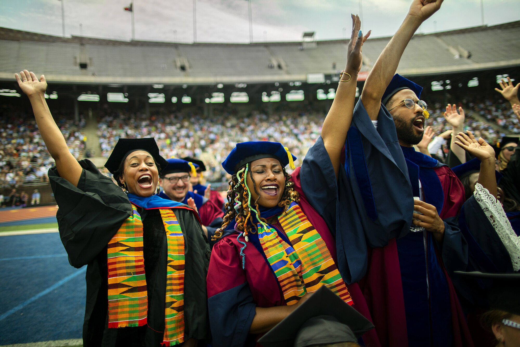 Three graduates stand with arms in the air, cheering.