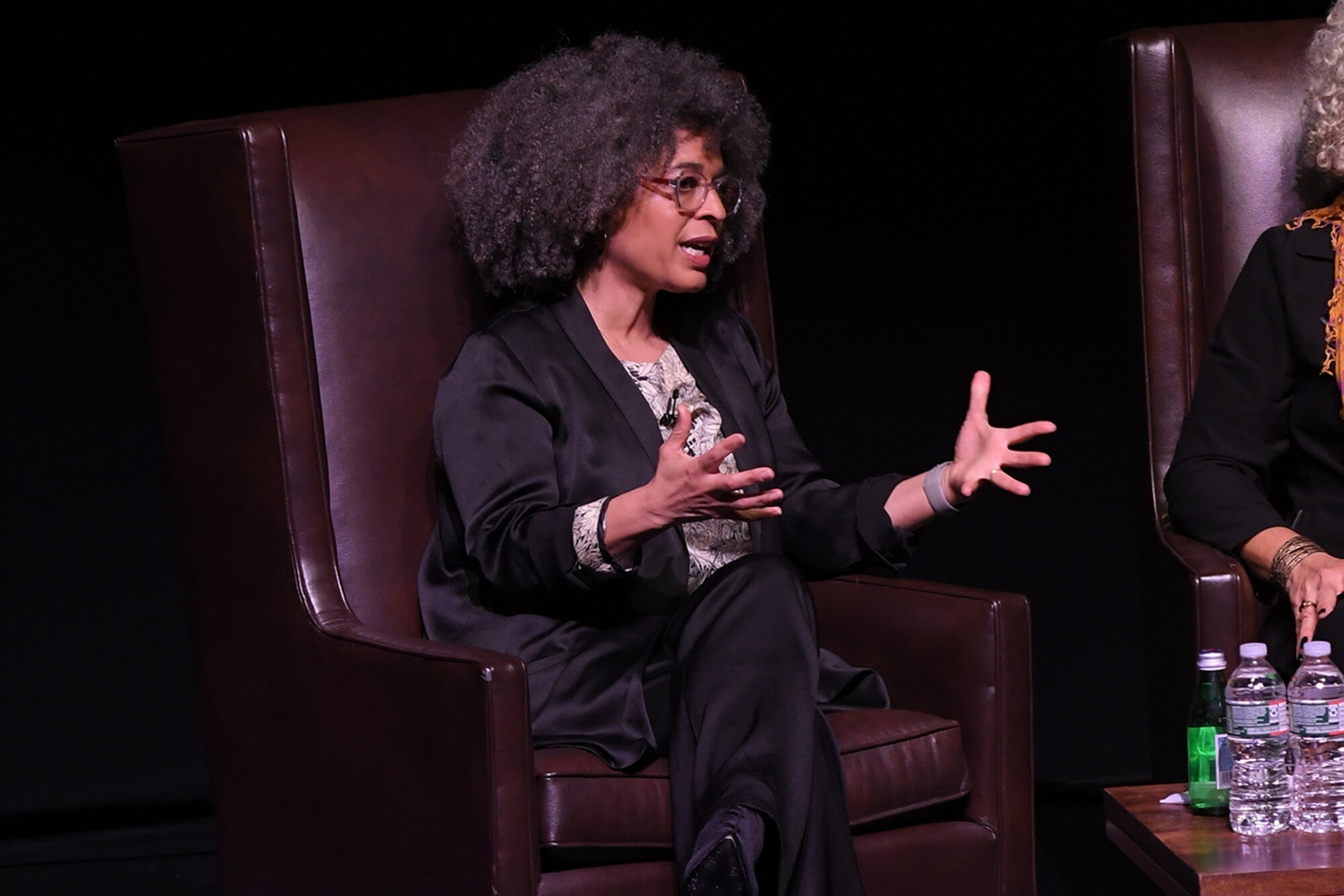 Gina Dent sits in a chair on stage with hands out in mid-sentence