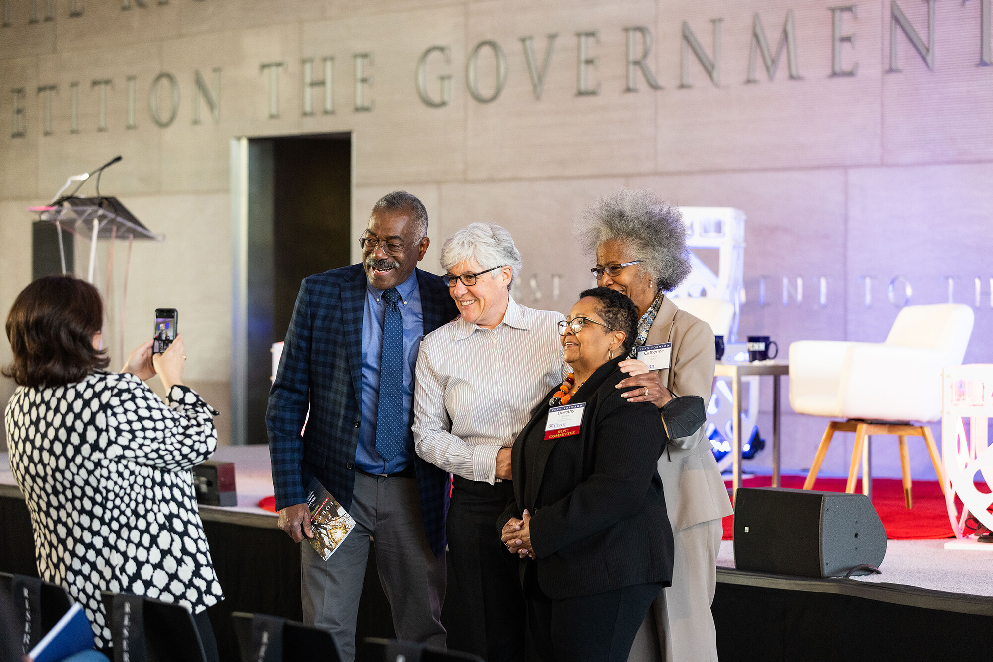 Photo of person taking an iPhone photo of four individuals smiling in front of stage at Constitution Center