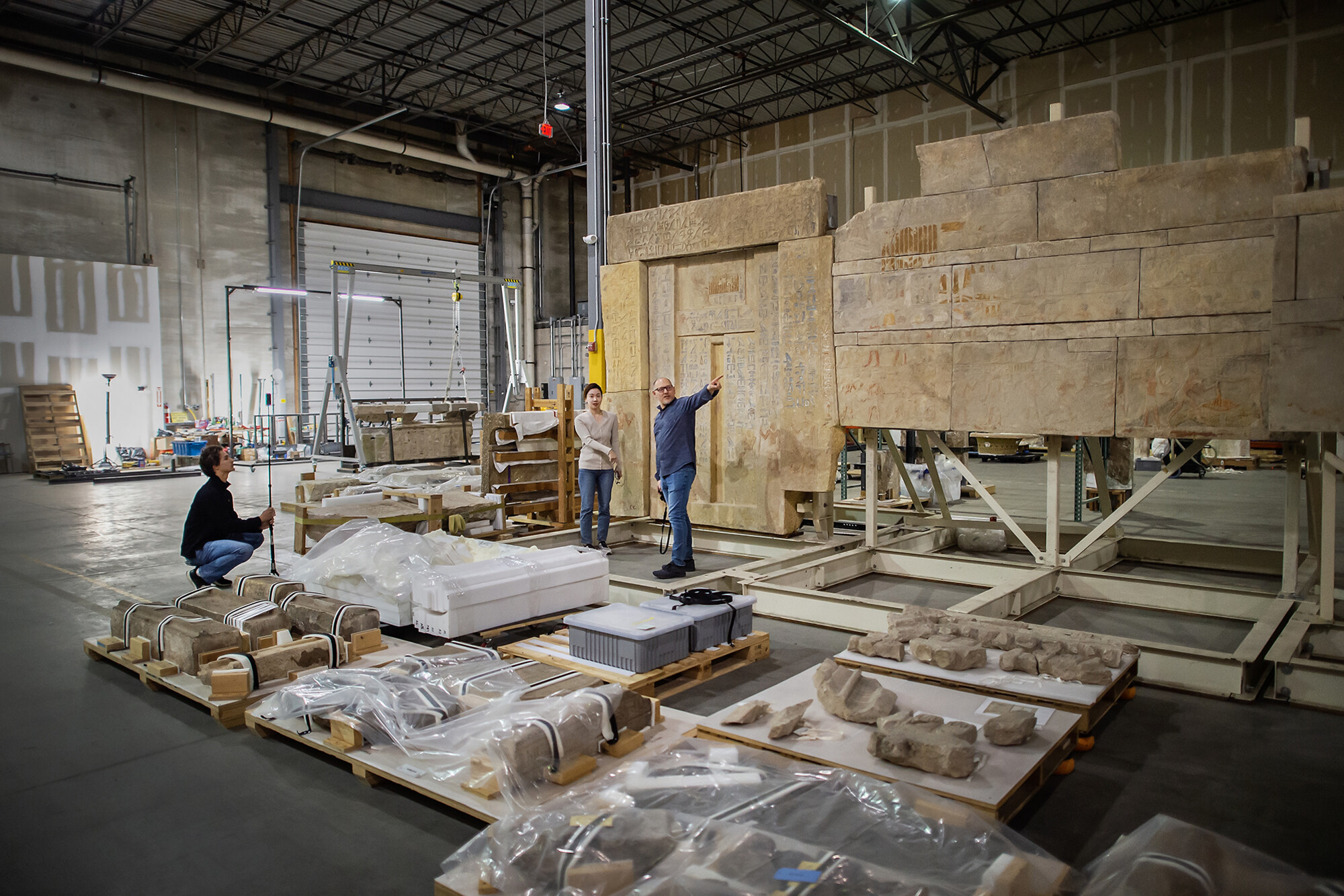 Peter Decherney and two students in a the Museum warehouse looking at many pallets of items laid out on the floor.