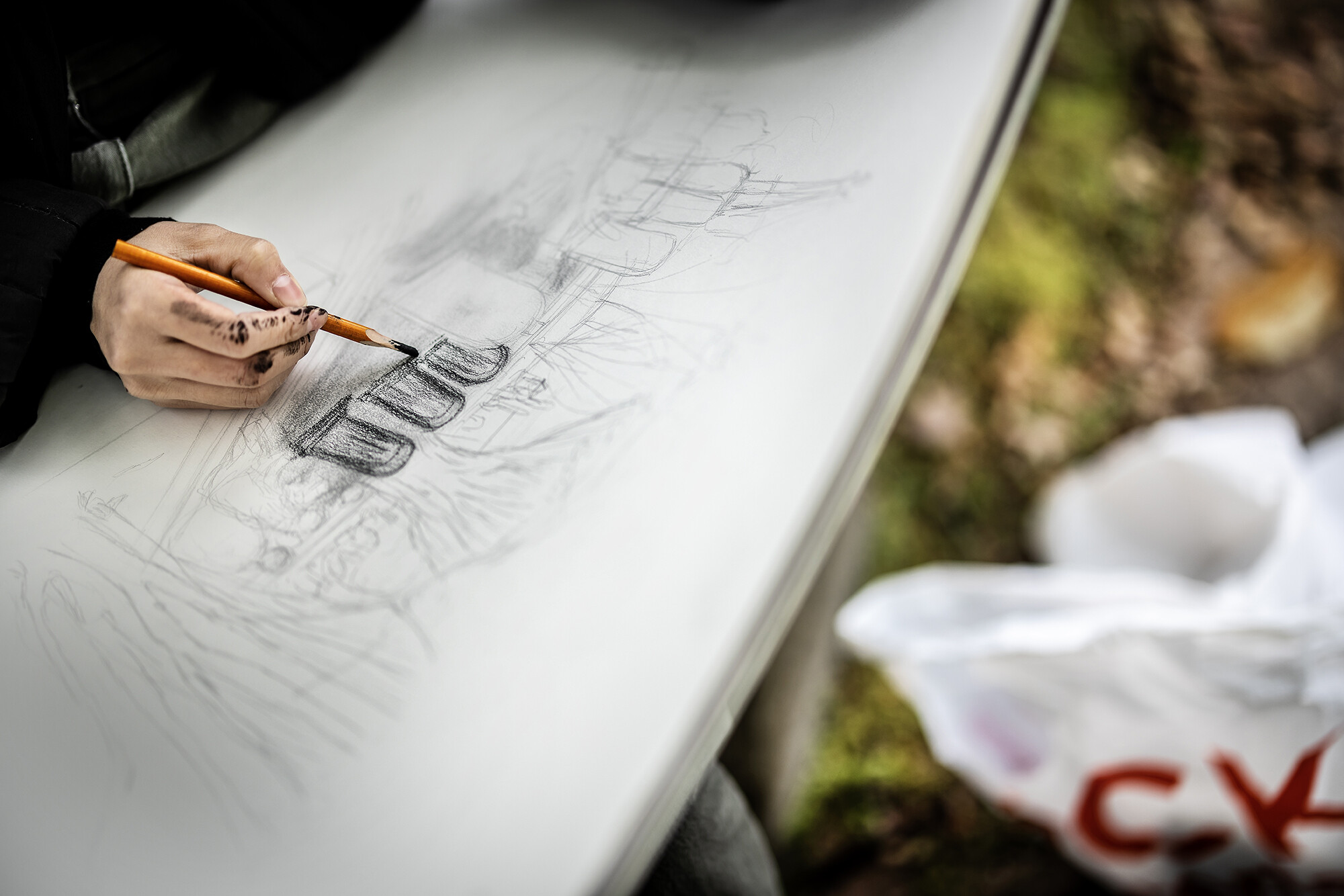 A hand drawing a landscape in charcoal.