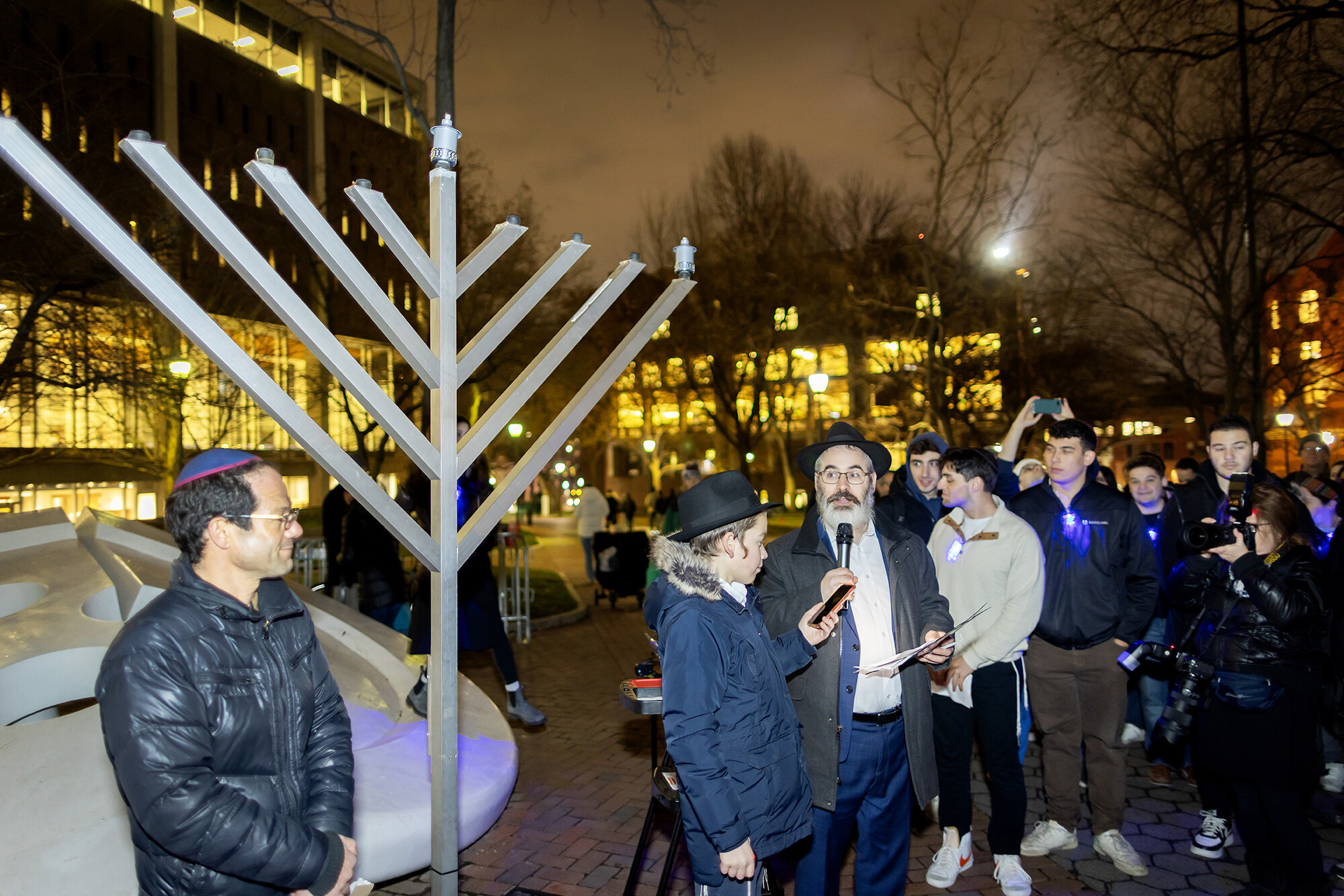 People speaking outside Van Pelt Library by a large menorah.