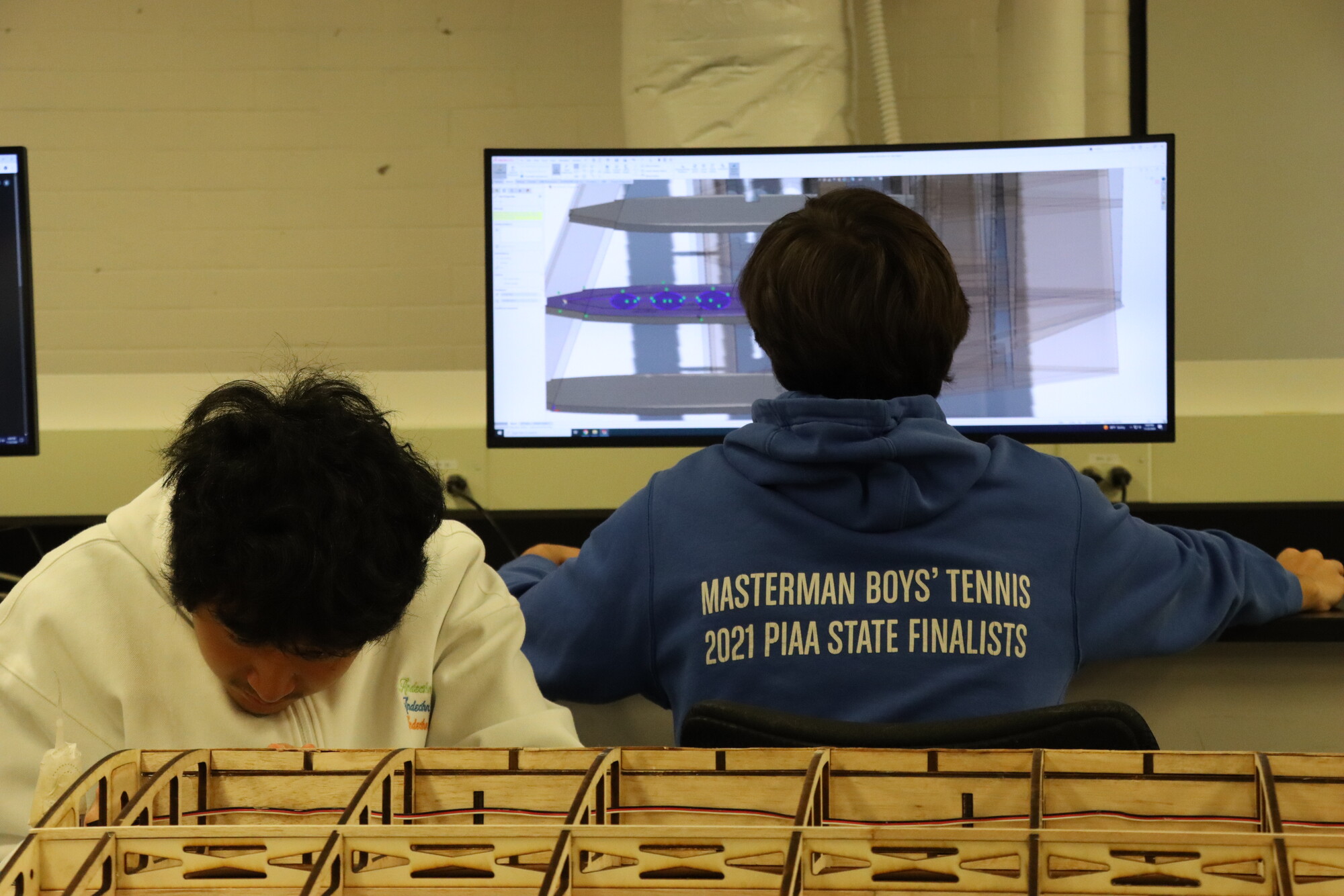 Two students working on building penn’s aerial racing drone, one on the parts themselves, one on a computer.