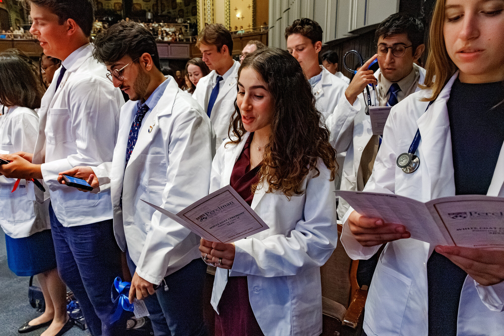 Doctors in white coats reading programs in the audience at Penn’s White Coat Ceremony.