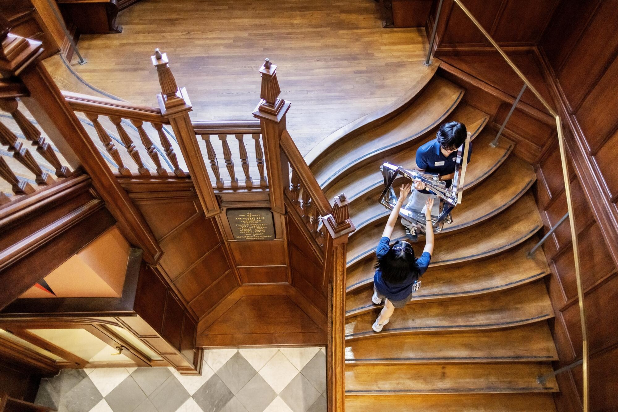 Two students carry Move-In supplies down an ornate Penn staircase.