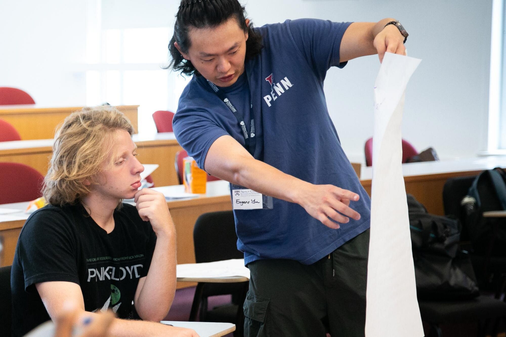 A person from Penn holding a long sheet of paper up to a student in a classroom.