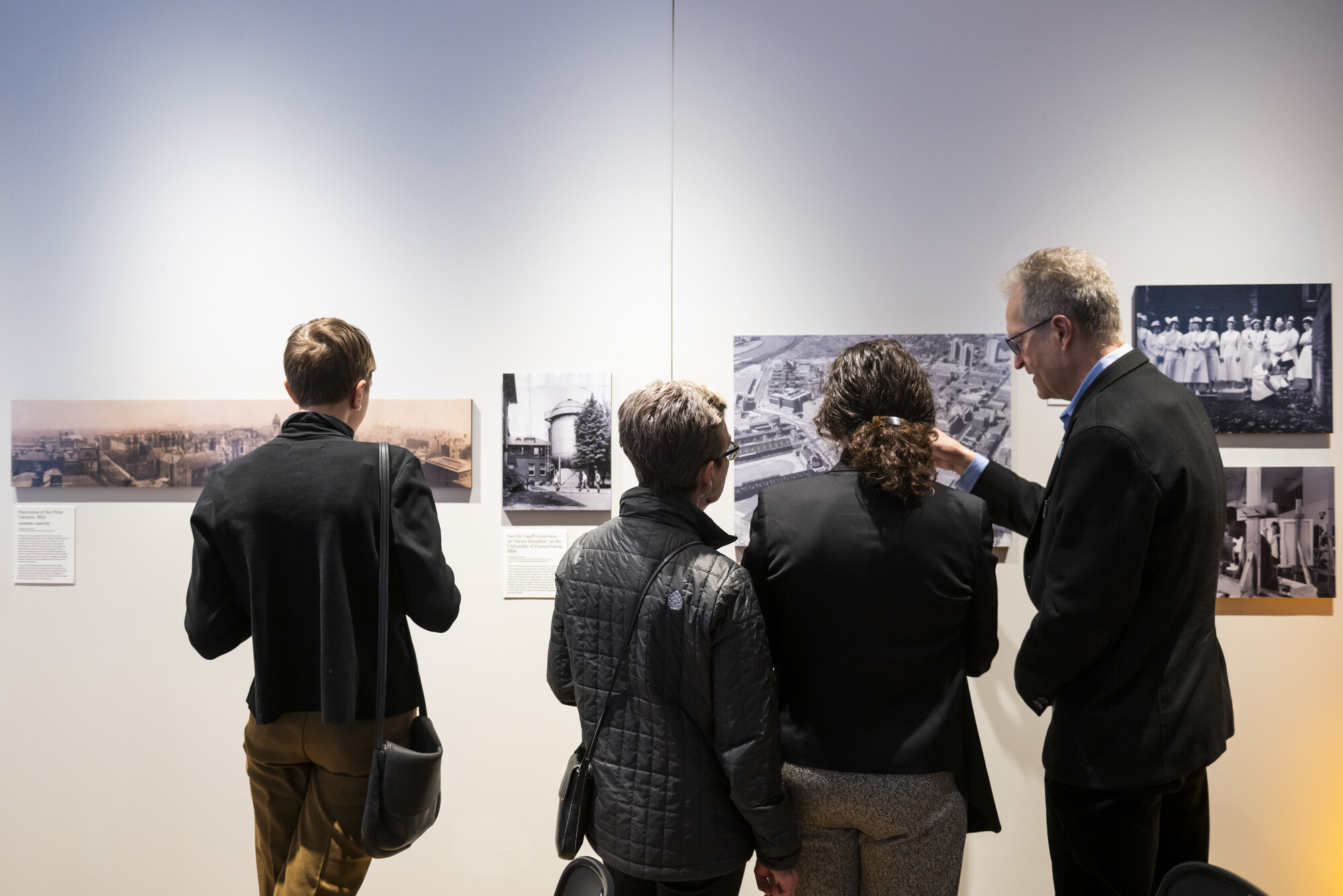 Four people looking at photographs displayed on the wall at Weitzman Hall.