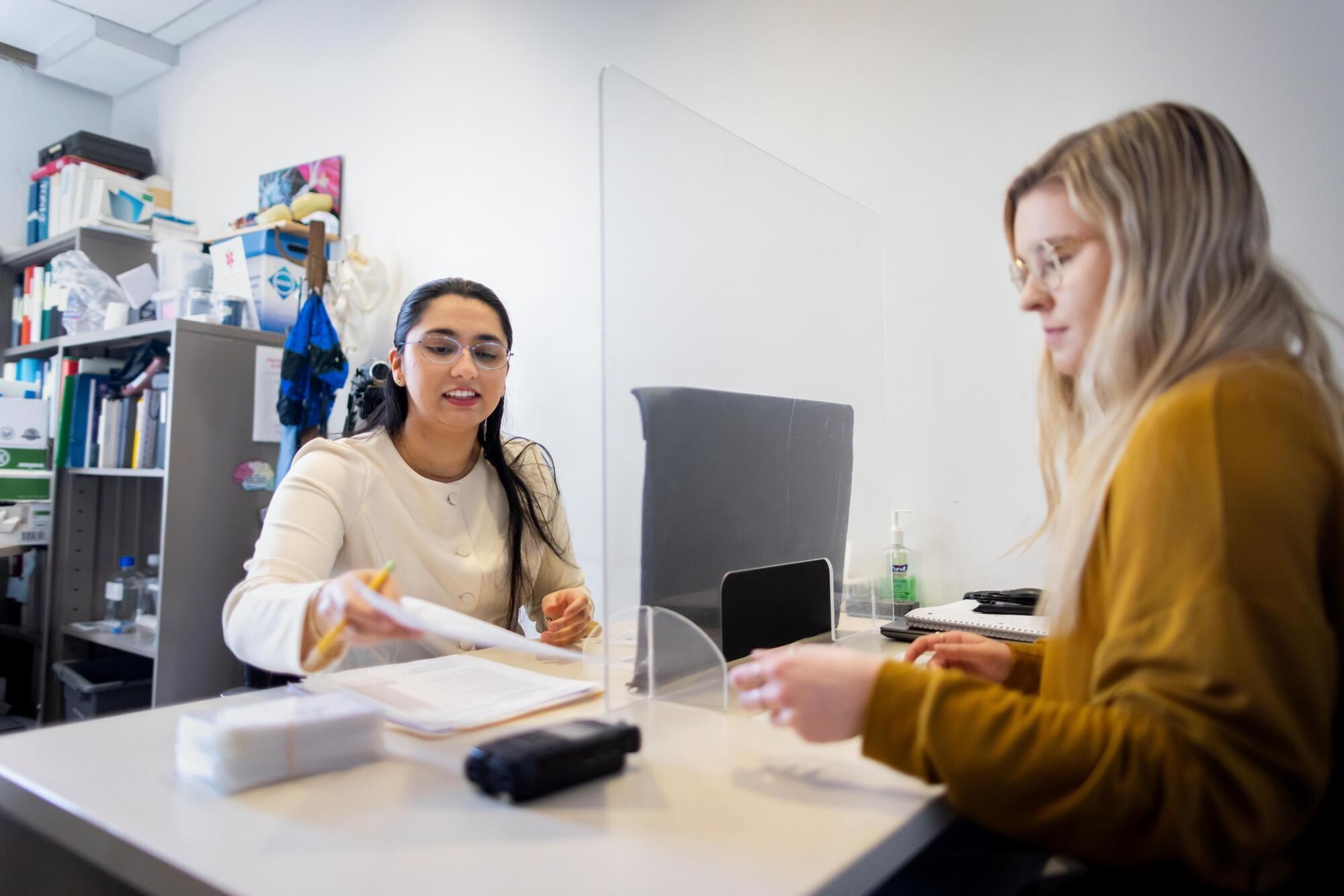 Shreya Parchure providing speech therapy counseling for a patient. They are seated at a desk and Parchure is handing the patient a paper form.