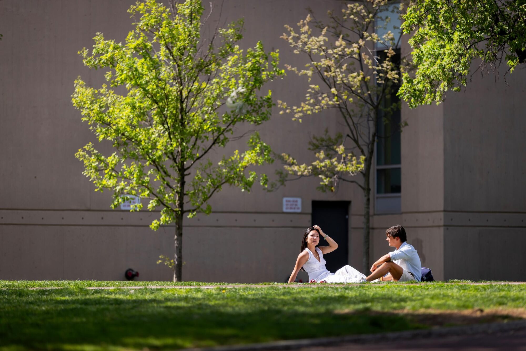 Two people sitting on the grass in front of a dorm on Penn’s campus.