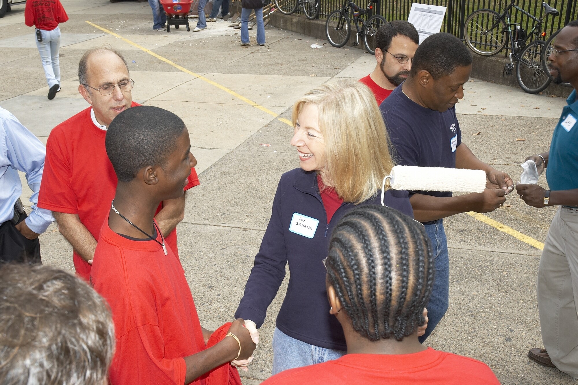 Ira Harkavy (left), Amy Gutmann (center), and Glenn Bryan (right) interacting with community members in an outdoor setting.