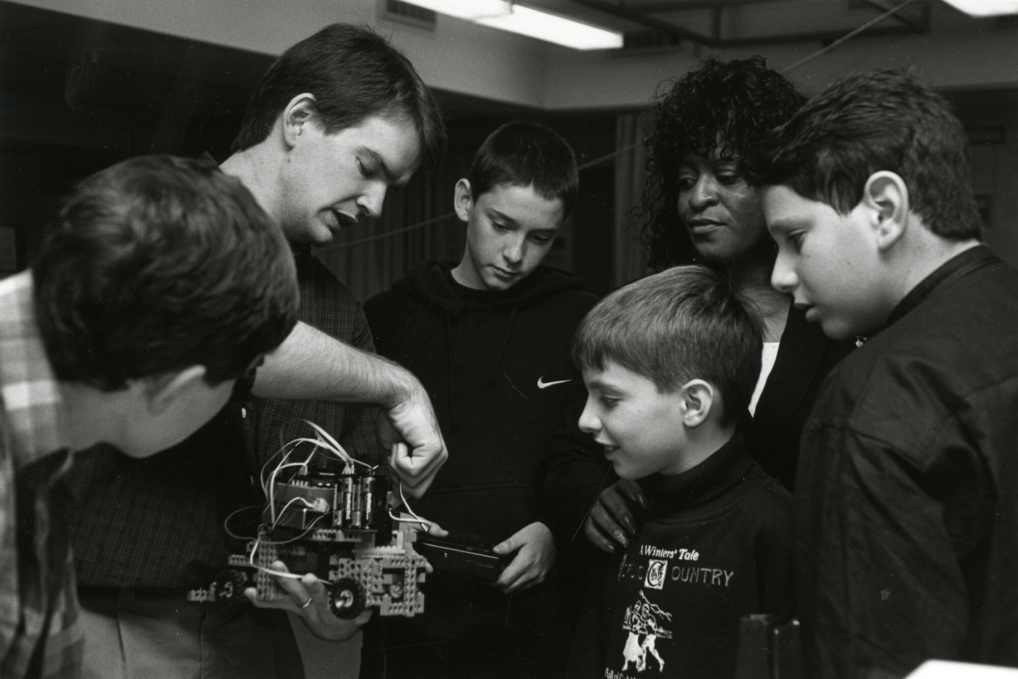 A Penn affiliate holding a robotic device. Young students and a teacher are surrounding the device and observing with interest.