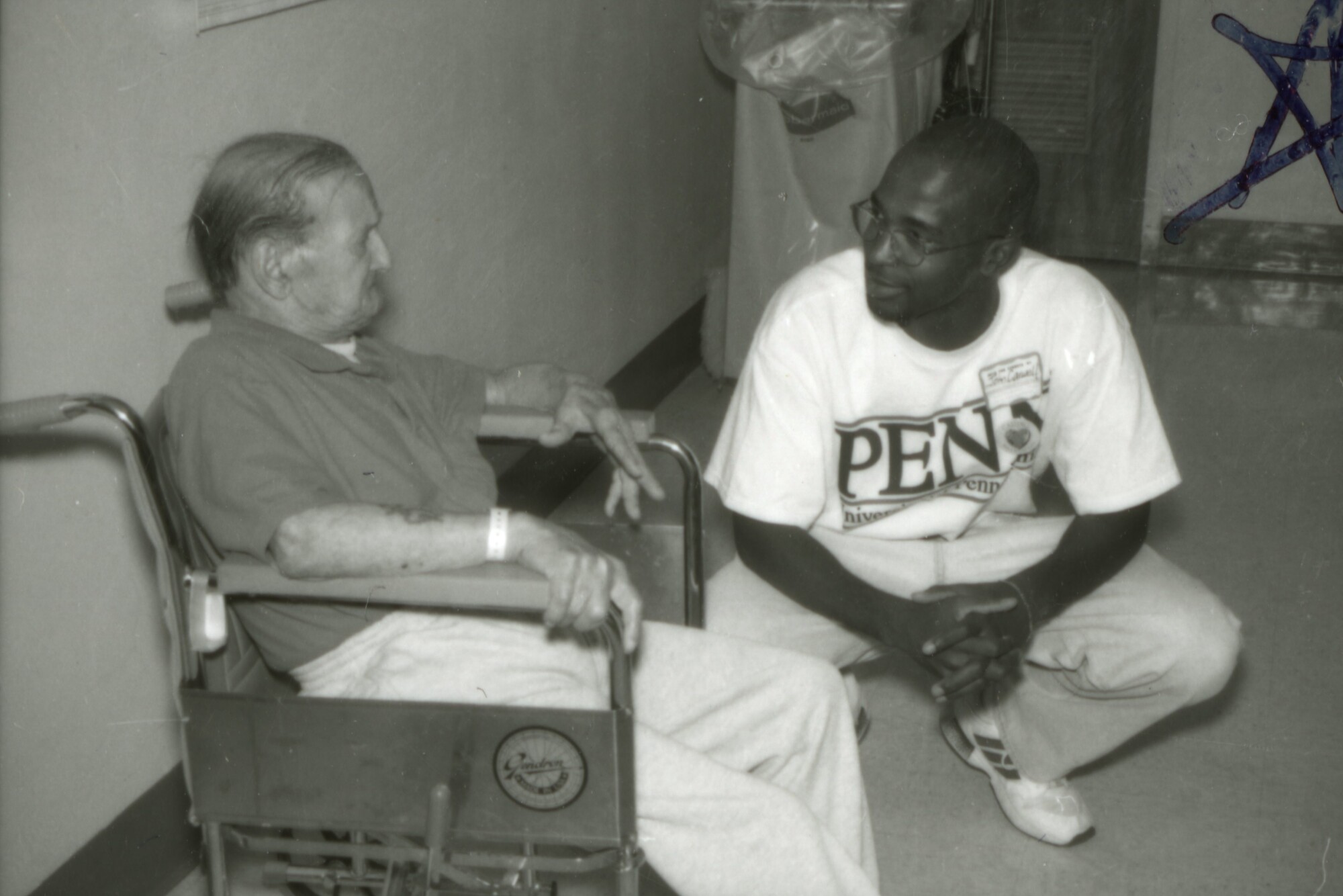 An older adult using a wheelchair (left) interacting with a Penn affiliate (right), who is wearing a Penn T-shirt.