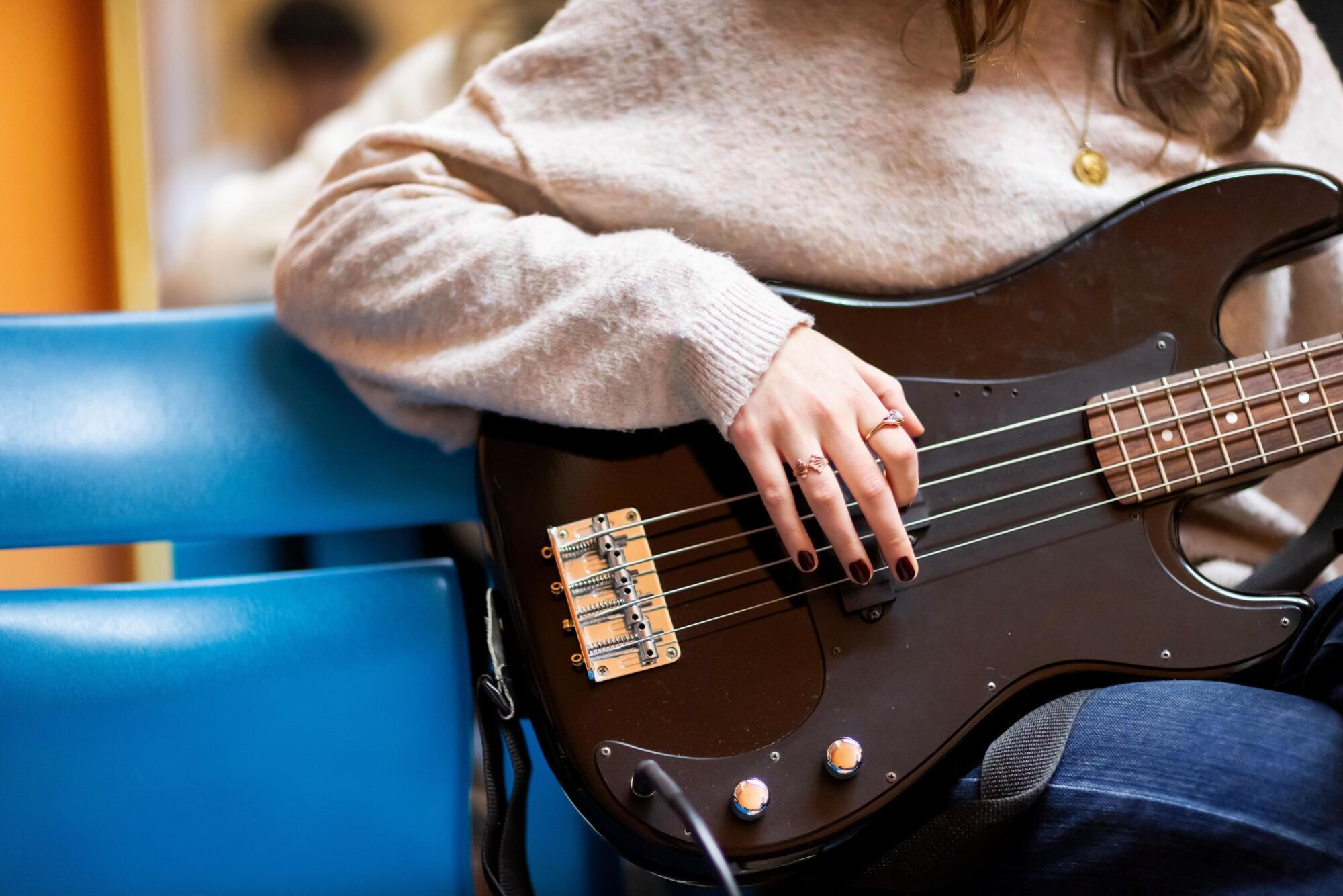 A student in the Bloomers band group is holding a guitar while strumming the instrument's strings. The student's face is not pictured.