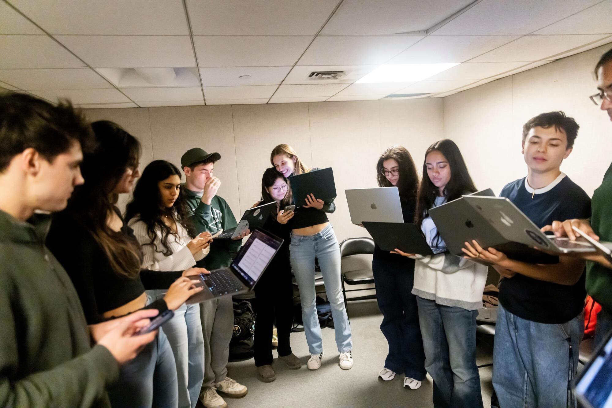 Students in the Dischord group circled around each other while holding laptops to review their music notes. They are preparing to practice their group number. In the image center, a pair of students is seen hugging each other and smiling.