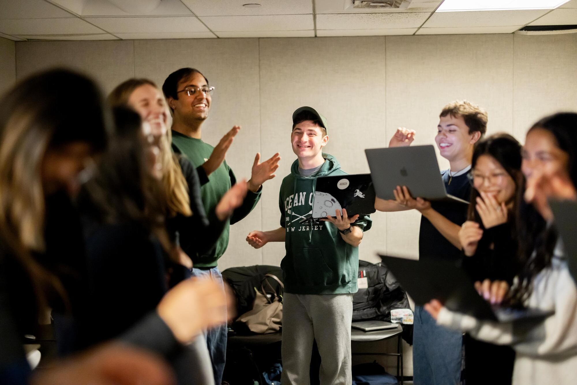 Students in the Dischord group practicing their a capella number. They are smiling, clapping, snapping, and laughing in unison, while holding laptops to follow the music notes.