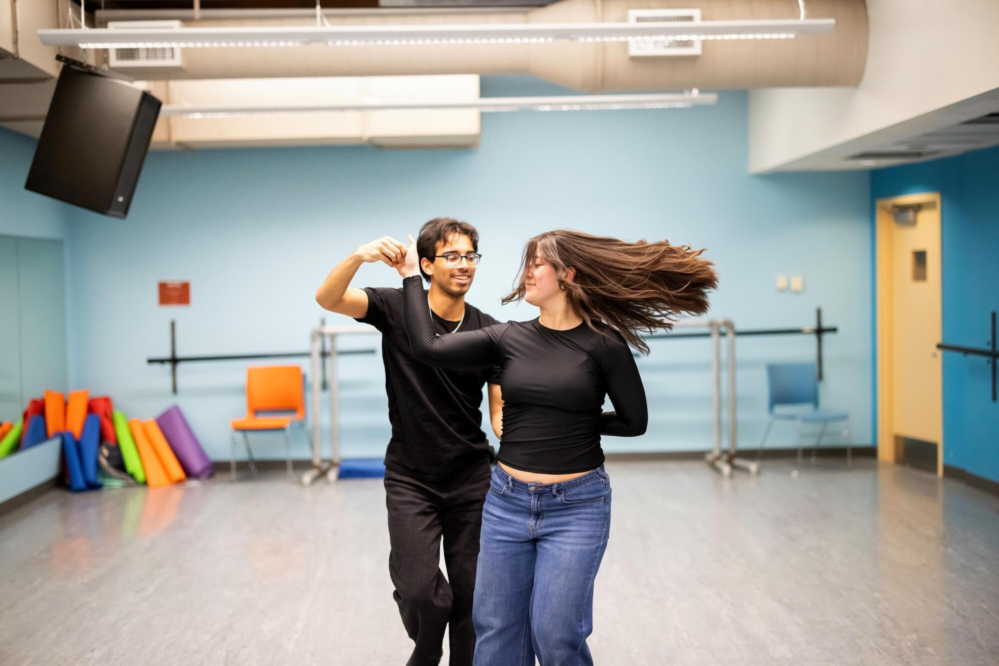 Two students in the Onda Latina group practicing a partner dance. On the left, the group lead is spinning a group member around (pictured right). The dancer on the right is pictured with long hair in motion while spinning around.