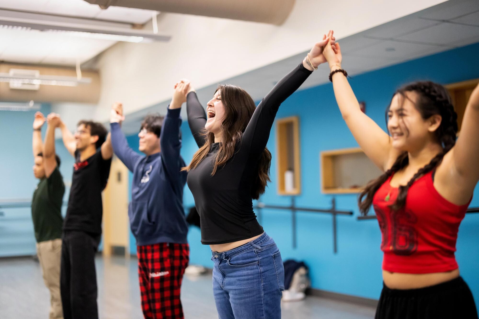 Students in the Onda Latina group are pictured smiling while holding hands in unison at the end of a practice routine. In the image center, one student is expressing a particularly exuberant, celebratory smile.