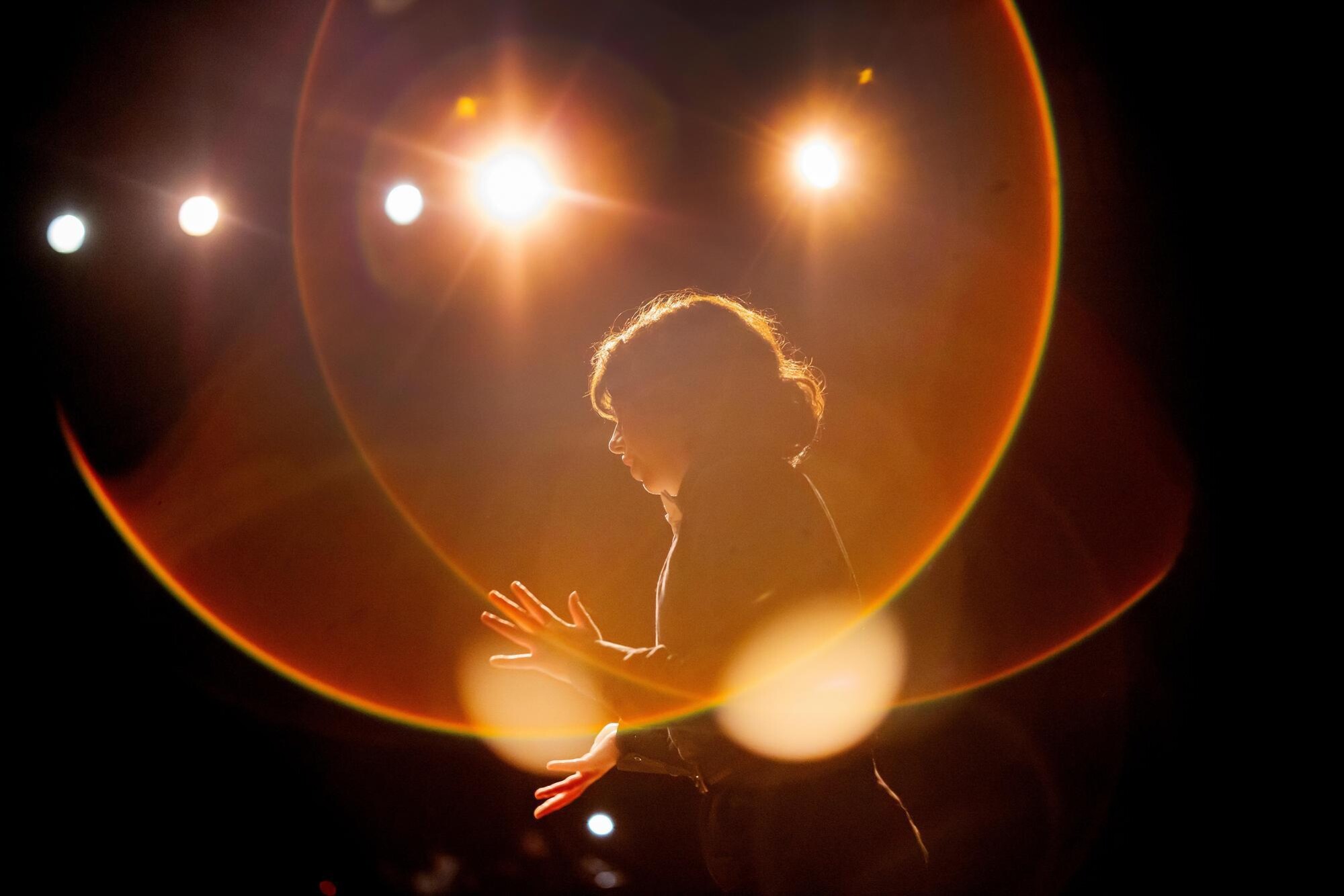 A student practicing their One Acts scene. They are illuminated by a red- and orange-tinted circular lighting glow.