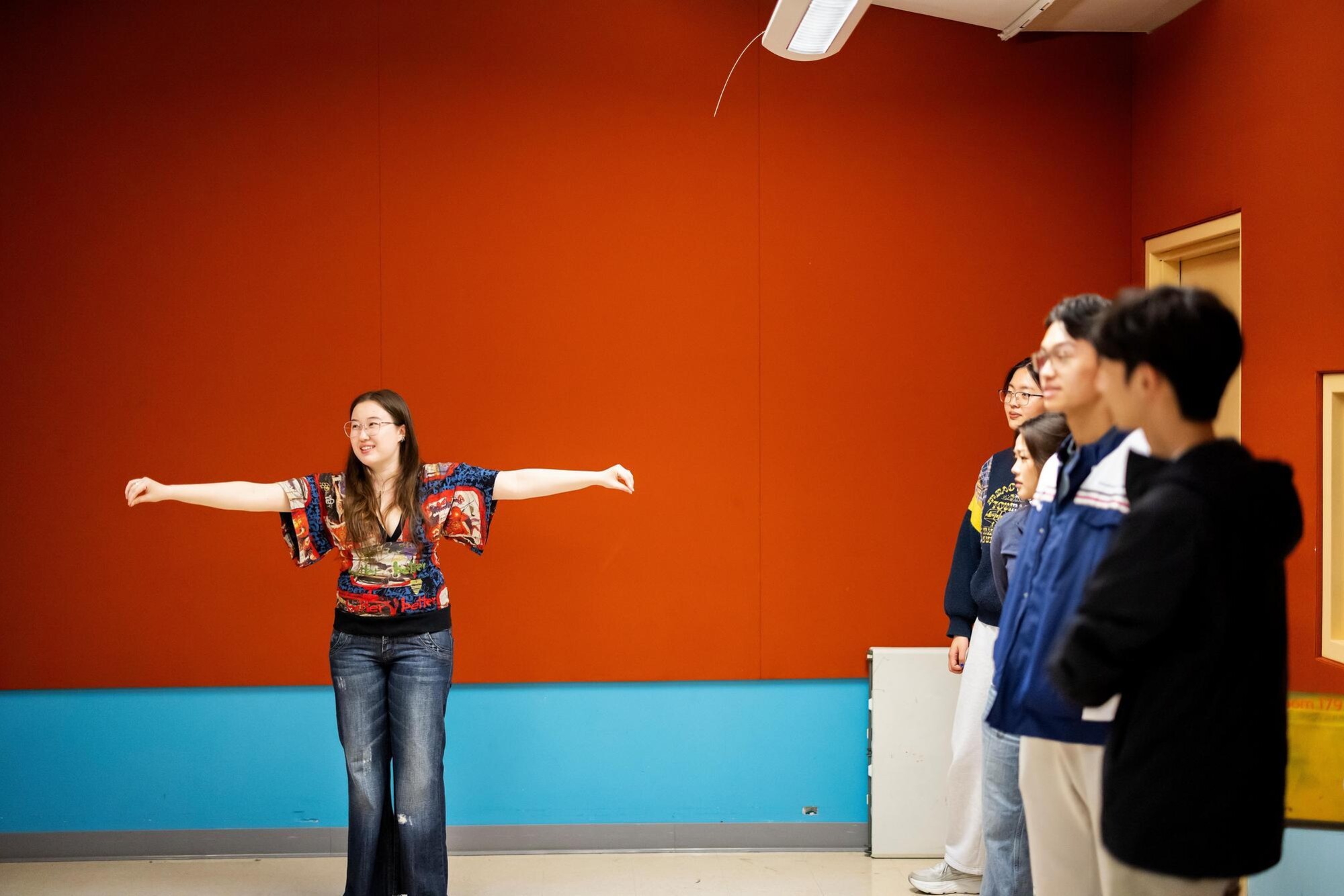 A student in the PennYo group is extending both arms outward. Four of their peers are standing to the right, watching the student practice.